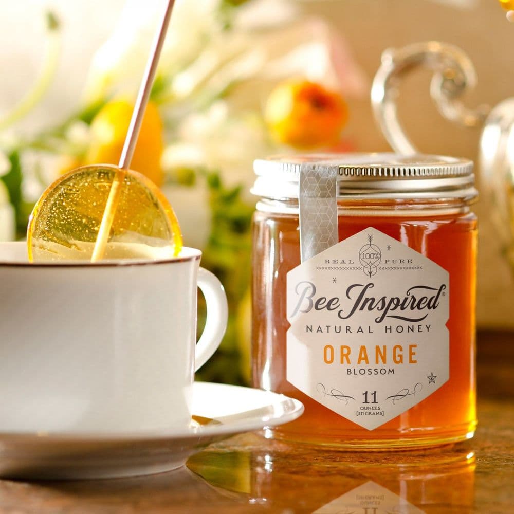 A Bee Inspired honey lollipop dissolving in a cup of tea, next to a jar of Bee Inspired honey
